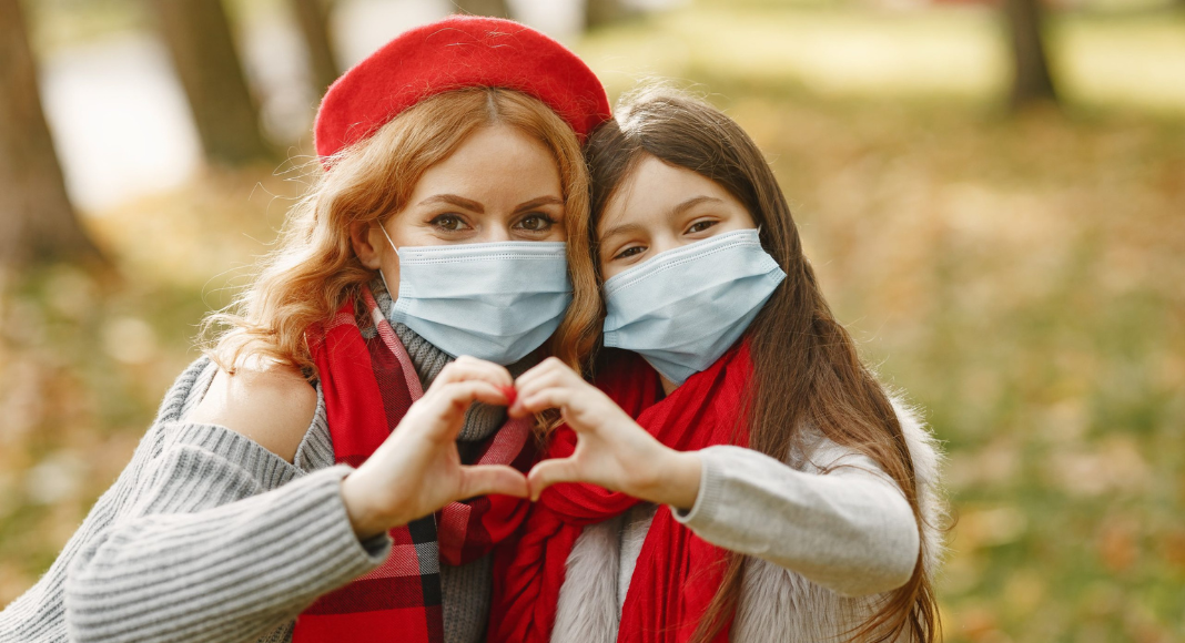 American heart month, Heart disease: A mom and her young daughter, dressed with red accessories, make a heart shape together with their hands.