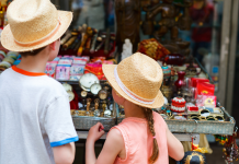 A young boy and girl in vintage hats look at a table filled with antiques.