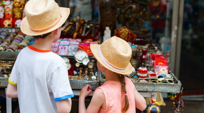 A young boy and girl in vintage hats look at a table filled with antiques.