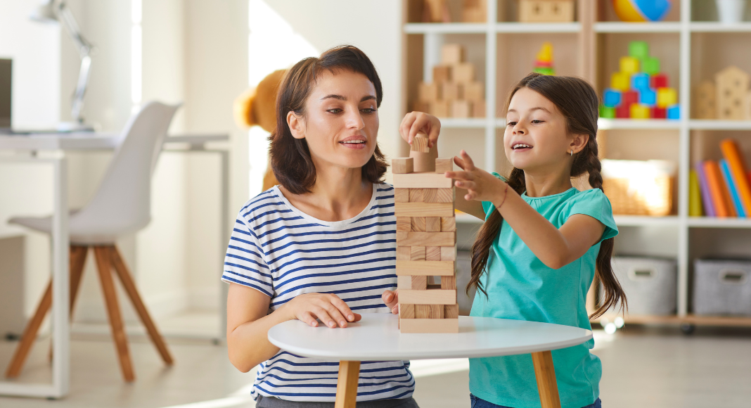 A mom and her young daughter play jenga together.