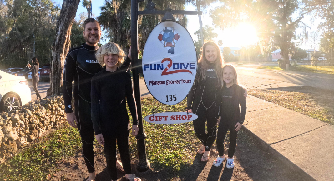 A family of four pose with a manatees swim tour sign.