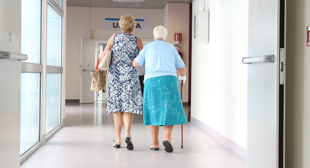 Elderly care: a middle-aged woman walks with an older woman with a cane.