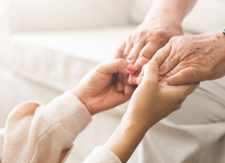 Elderly care: A young woman's hands hold those of an elder man.