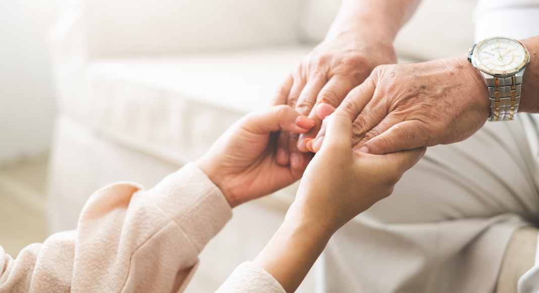 Elderly care: A young woman's hands hold those of an elder man.