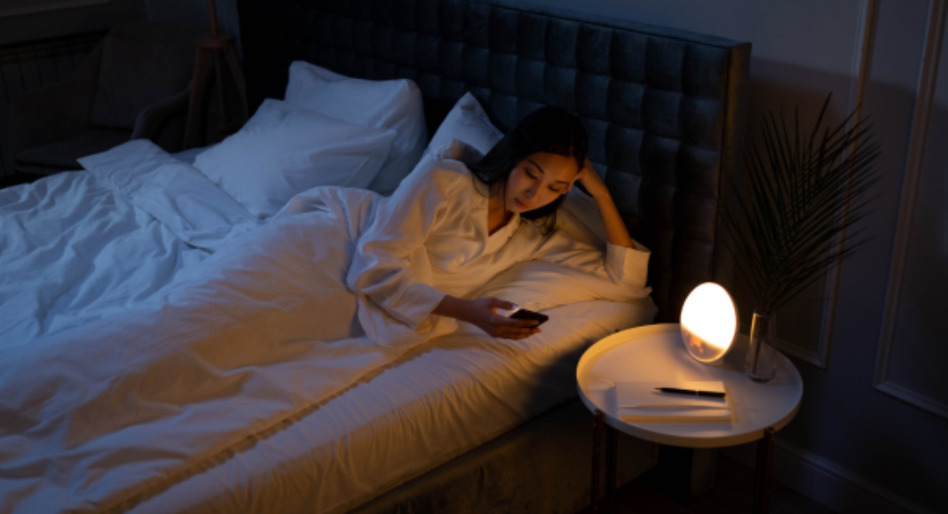 A woman in bed with the lights out, scrolling on her phone.