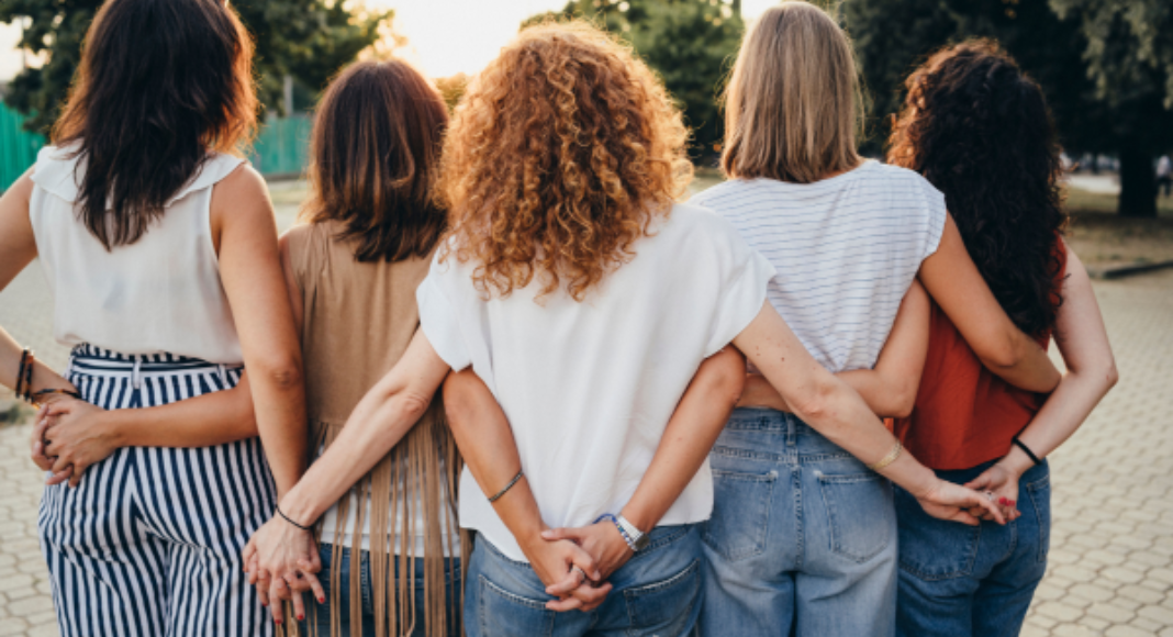 A group of women stand with their arms around each other.