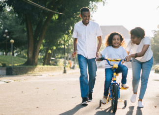 foster care crisis: two parents help a young girl with riding her bike.