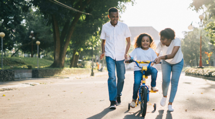 foster care crisis: two parents help a young girl with riding her bike.