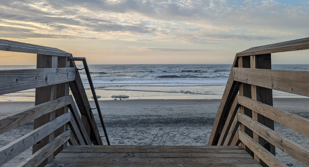 date ideas folly beach: a view of the ocean from the pier steps with a cloudy sunset overhead.