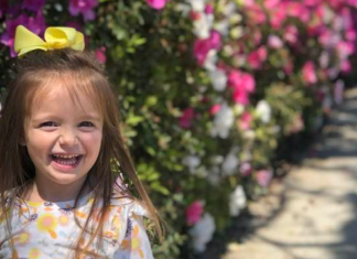 A little girl smiles in front of bushes of azaleas.