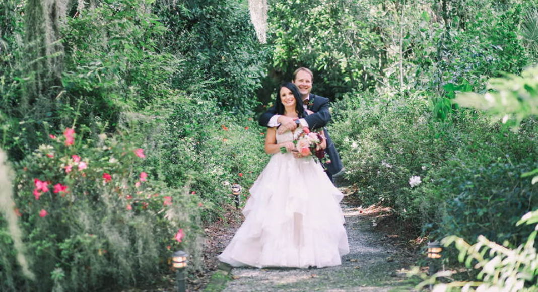 A couple on their wedding day amid a green landscape with pink flowers.