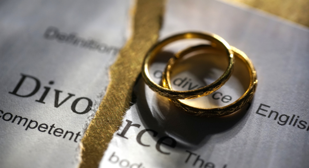 A dictionary page defining the word Divorce is torn in two, with wedding rings piled on top.