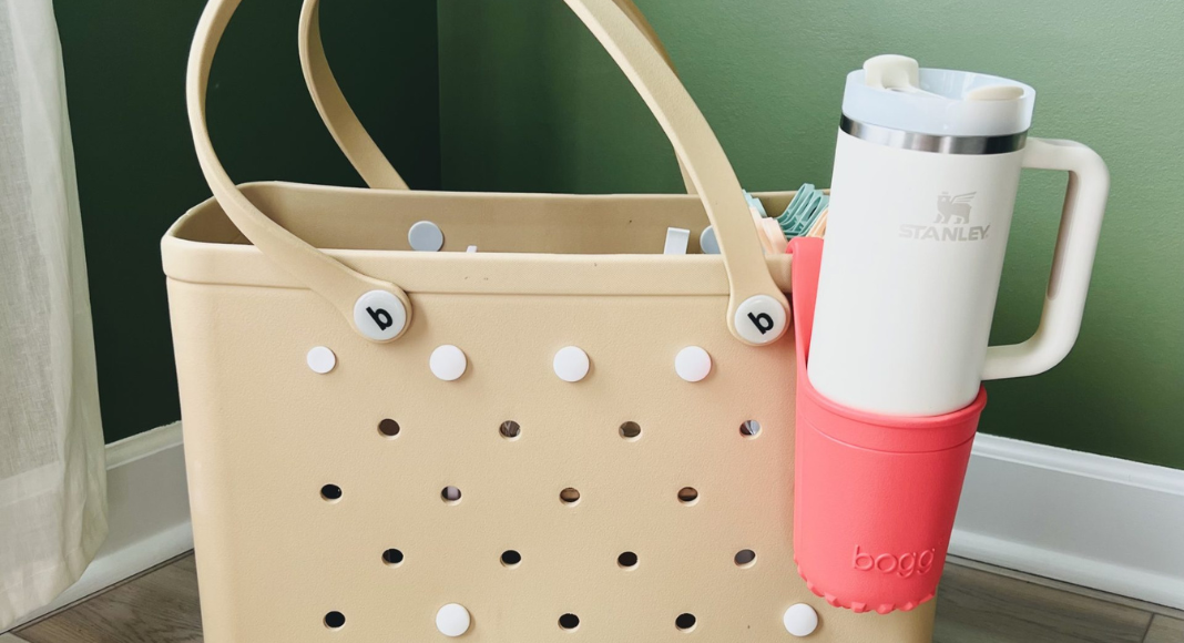 Pool day essentials: a tan bogg bag with a white stanley cup attached with a pink cup holder.