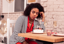 Birthday hum: a woman sitting at a restaurant table stares down sadly at a small birthday cake.