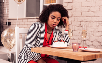 Birthday hum: a woman sitting at a restaurant table stares down sadly at a small birthday cake.