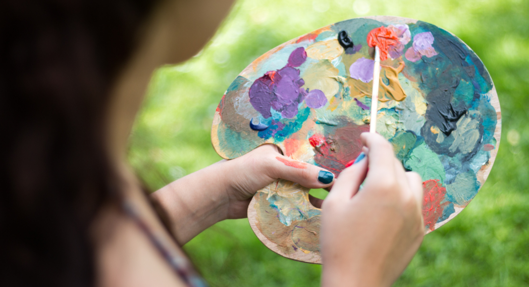 A girl holds a paint palette outside to spend more time outside.