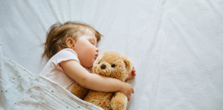 A toddler sleeping in bed with her teddy bear.