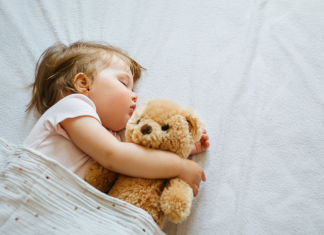 A toddler sleeping in bed with her teddy bear.