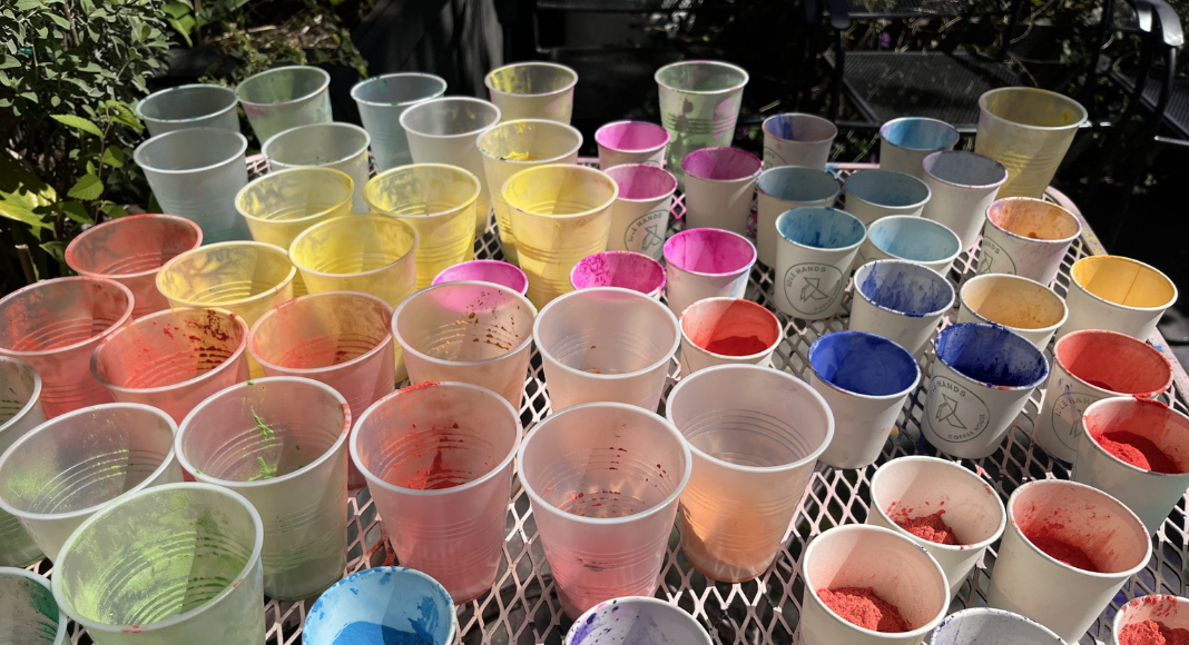 Colored powders in plastic cups on a table at a Holi celebration.