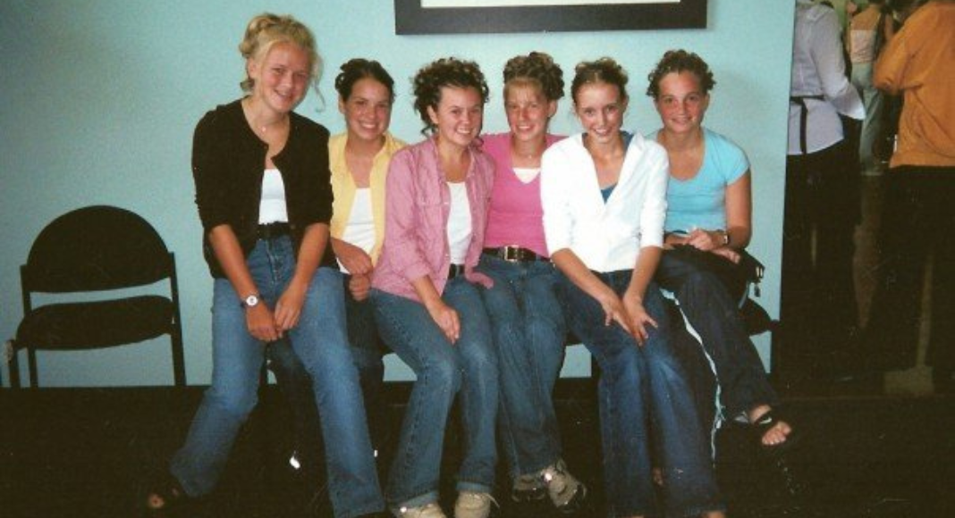 A group of 6 high school girls take a picture on a bench after prom with comfy clothes and their hair done up.