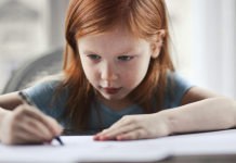 Encourage a young writer: a little girl writes at a table with a very focused expression.