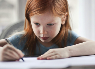 Encourage a young writer: a little girl writes at a table with a very focused expression.