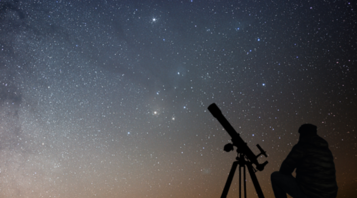 National Space Day: a silhouette of a person with a telescope set up to view the starry night.