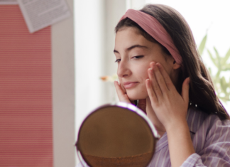skincare for children: a young teen girl applies skincare products to her face in front of a mirror.
