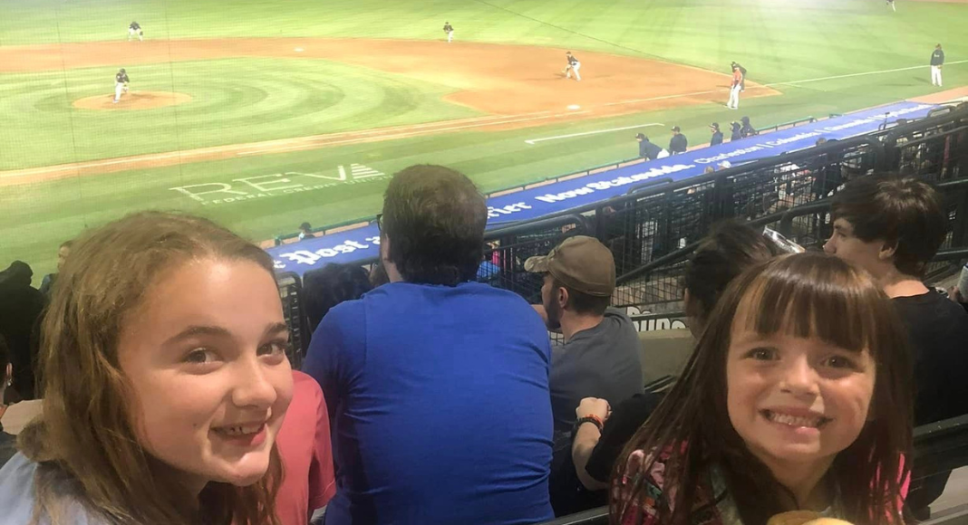 Things to do in Charleston with teens: a teen girl and young girl smile together at a baseball game.