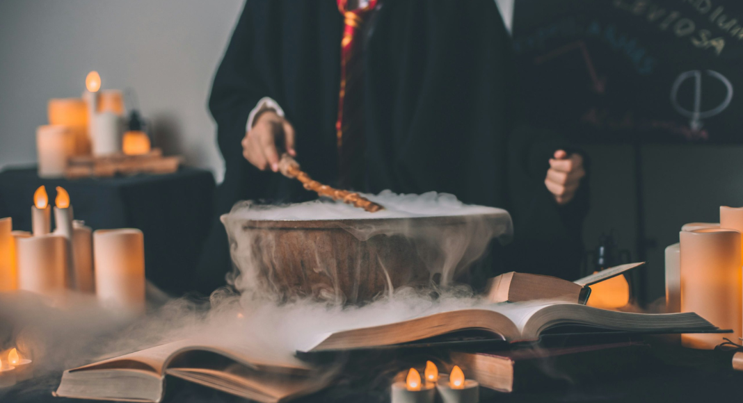 A wizard student mixes in a cauldron, with candles and books open around him.