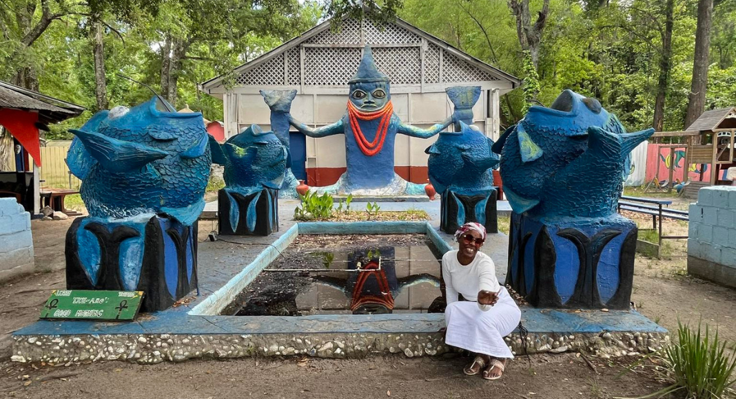 A woman at Oyotunji African Village sits with 5 blue fish-related statues.