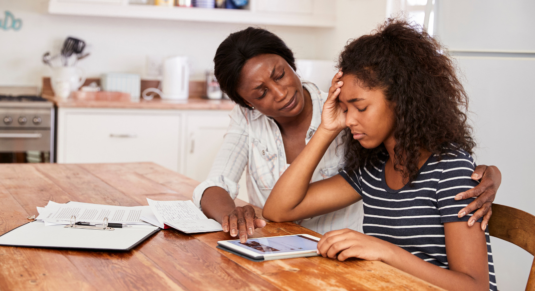 Teen stress: a mother comforts her stressed out teenage daughter at the table with homework strewn about.