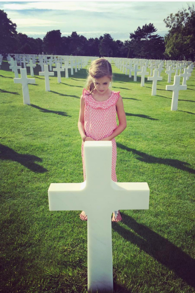 D-Day: a young girl stands in front of a white cross at a grave in the American Cemetery in Normandy