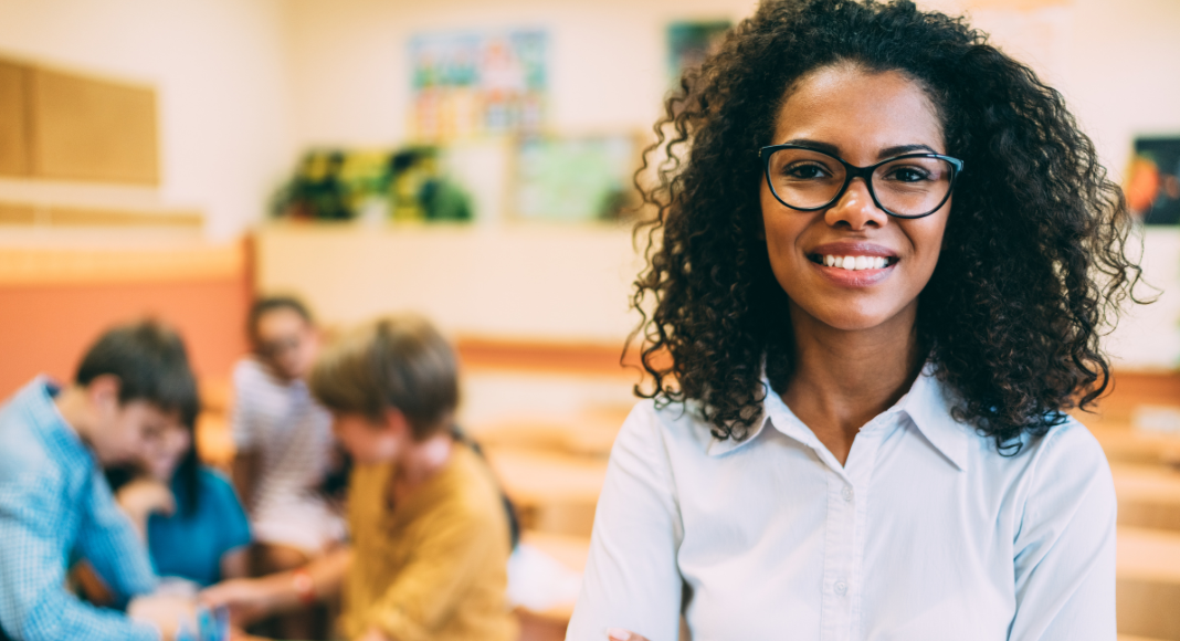 teacher appreciation week gifts: A teacher smiles, with a small group of students working on a project together in the background.