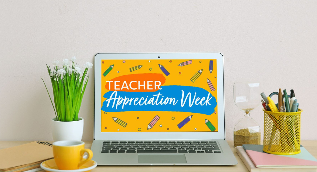 A laptop open that reads, "teacher appreciation week." Surrounding it are a cup of pens, notebooks, a tea cup and saucer, and small plant on top of the desk.