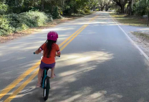 girlhood: a girl wearing a pink helmet rides her bike on an empty road.