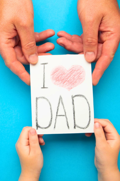 A child and Father's hands hold a card that says "I love Dad."